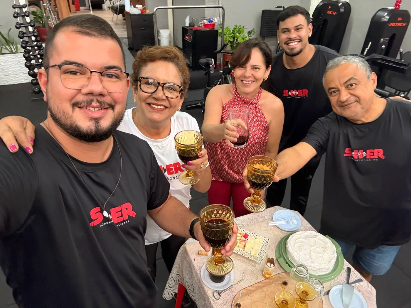 Pessoas reunidas ao redor de uma mesa com bolo na Sher