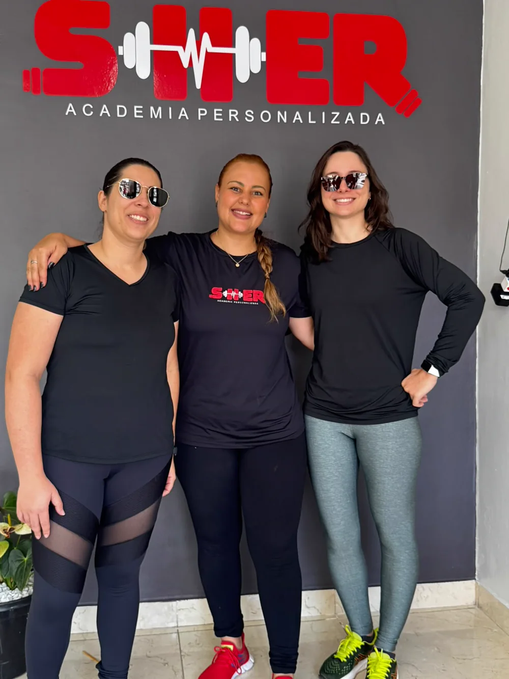 Três mulheres reunidas em frente à marca Sher